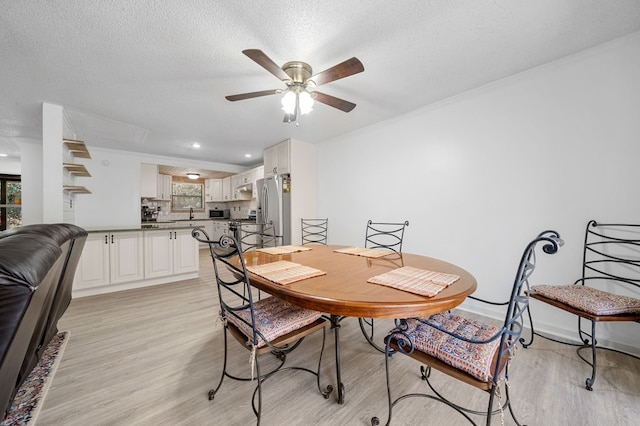 dining room featuring a ceiling fan, baseboards, light wood-type flooring, and a textured ceiling