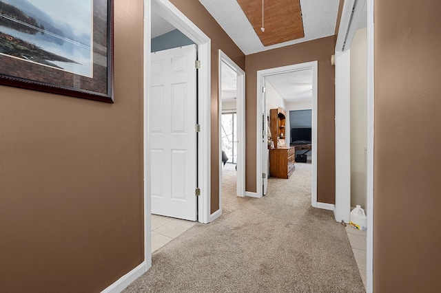 hallway with baseboards, light carpet, and attic access