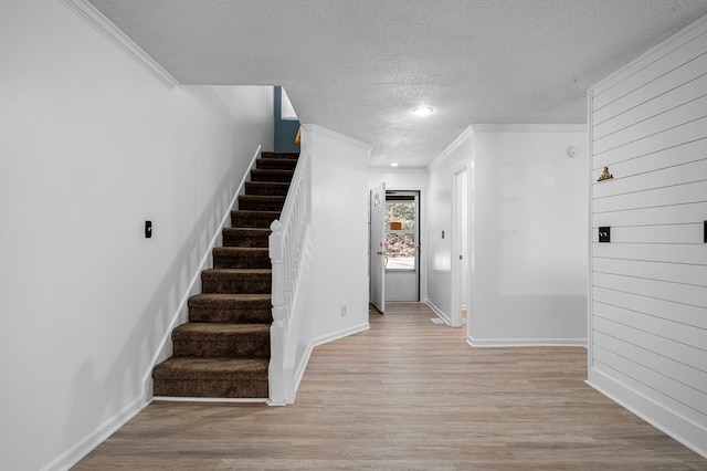 stairs featuring a textured ceiling, crown molding, baseboards, and wood finished floors