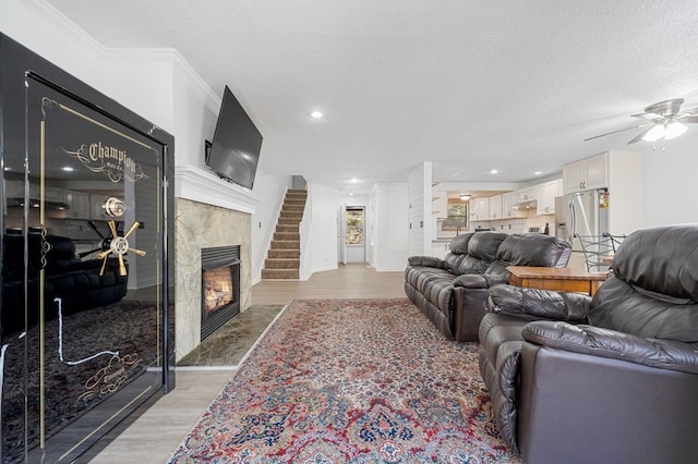 living area with light wood-type flooring, a textured ceiling, a fireplace, and a ceiling fan