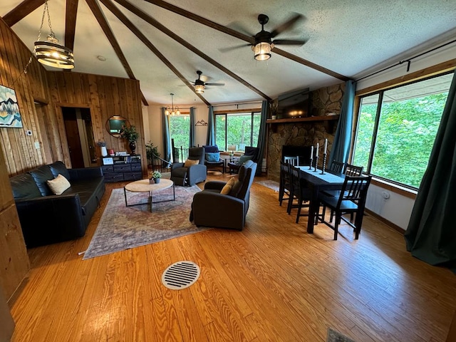 living room with a stone fireplace, hardwood / wood-style flooring, lofted ceiling with beams, and a textured ceiling