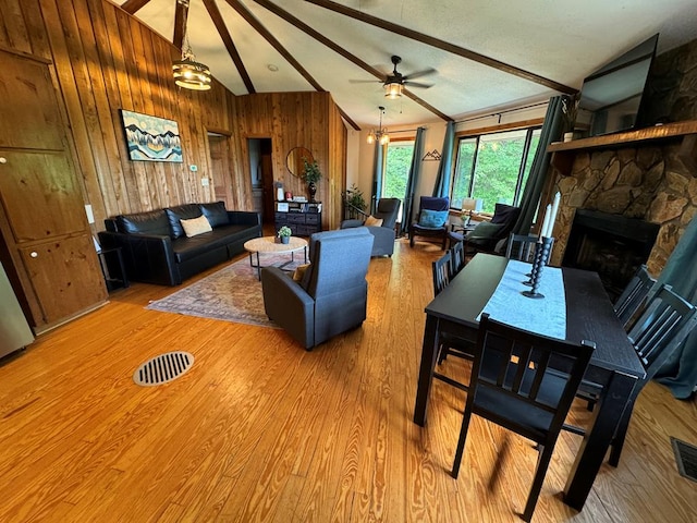 living room with a stone fireplace, wood walls, vaulted ceiling with beams, and light wood-type flooring