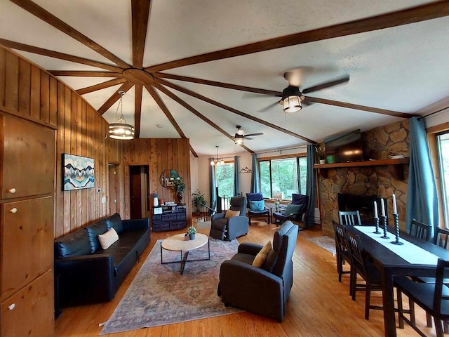 living area featuring a stone fireplace, wood walls, vaulted ceiling with beams, and wood finished floors