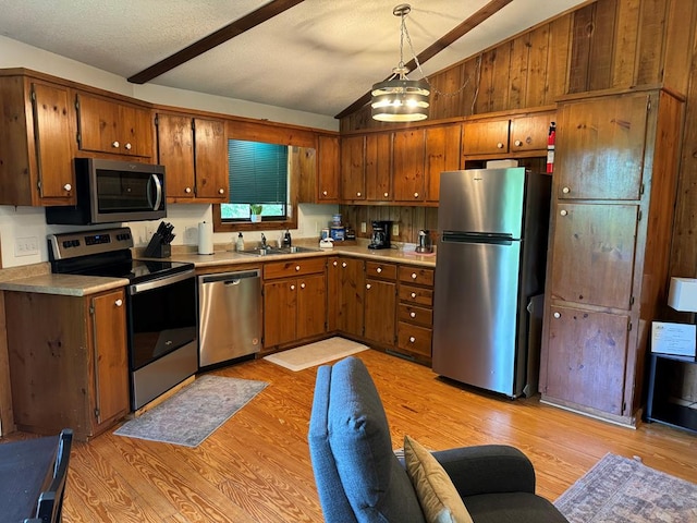 kitchen featuring lofted ceiling, stainless steel appliances, light hardwood / wood-style floors, pendant lighting, and sink