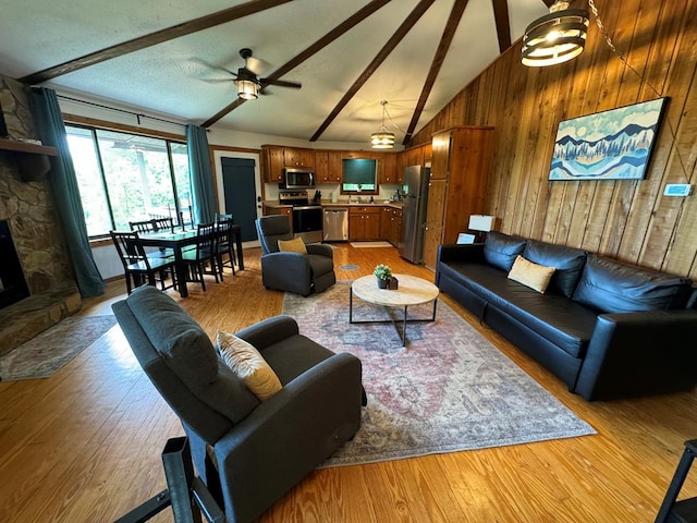 living area featuring wooden walls, lofted ceiling with beams, light wood-style flooring, a fireplace, and a ceiling fan