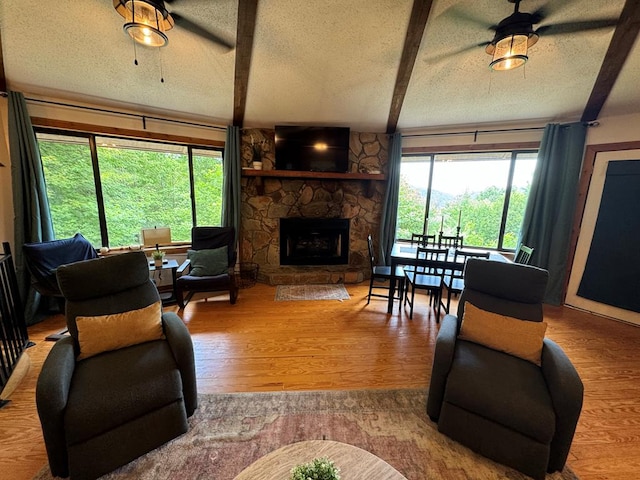 living area with wood finished floors, a textured ceiling, a stone fireplace, and ceiling fan