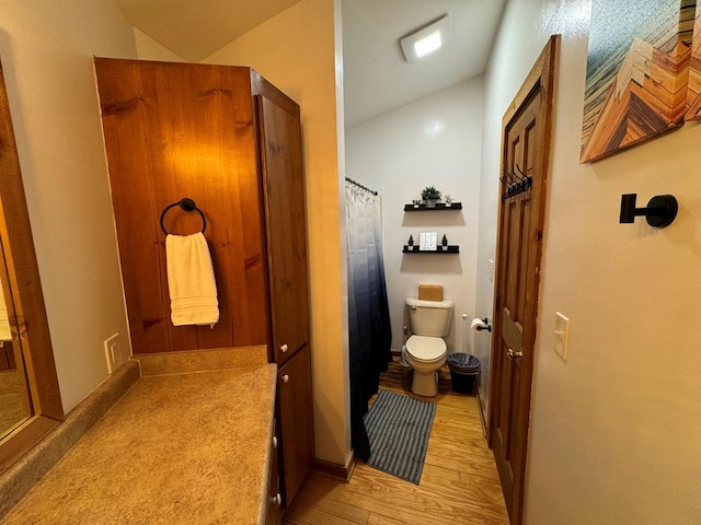 bathroom featuring a shower with shower curtain, toilet, wood finished floors, and vaulted ceiling