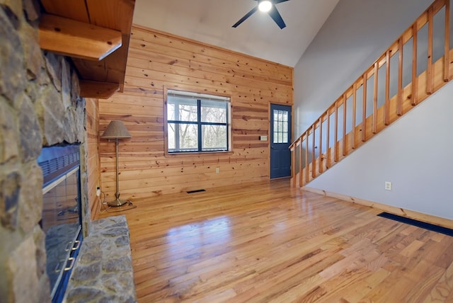 unfurnished living room with ceiling fan, high vaulted ceiling, wooden walls, and light hardwood / wood-style floors