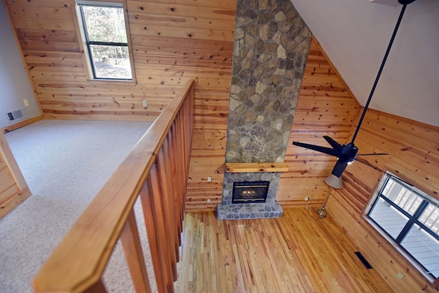 unfurnished living room with a fireplace, wooden walls, light hardwood / wood-style floors, and a towering ceiling