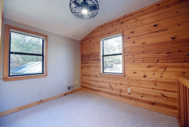 spare room featuring vaulted ceiling, carpet, and wood walls