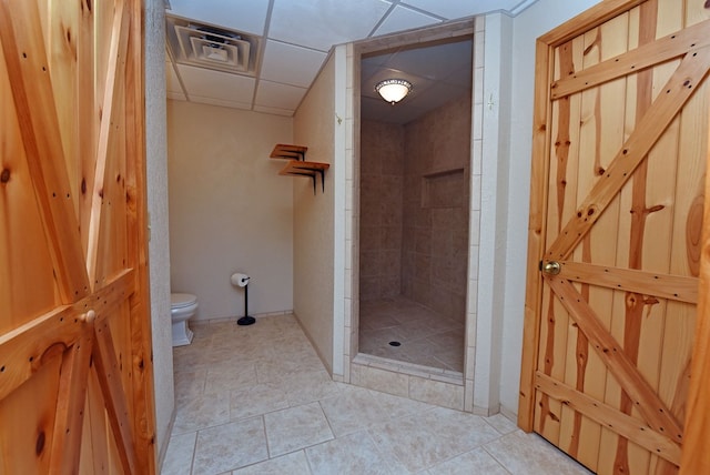 bathroom with a tile shower, tile patterned flooring, a paneled ceiling, and toilet