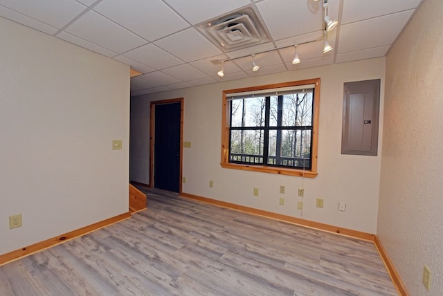 unfurnished room with track lighting, electric panel, light hardwood / wood-style floors, and a drop ceiling