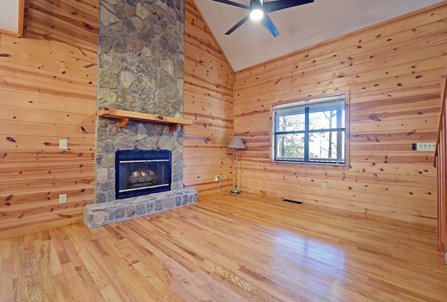 unfurnished living room with wood walls, high vaulted ceiling, ceiling fan, a fireplace, and hardwood / wood-style floors