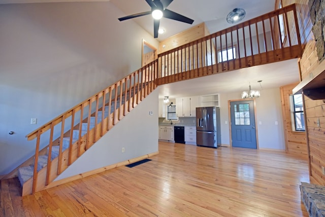 unfurnished living room featuring sink, ceiling fan with notable chandelier, light hardwood / wood-style flooring, and a high ceiling