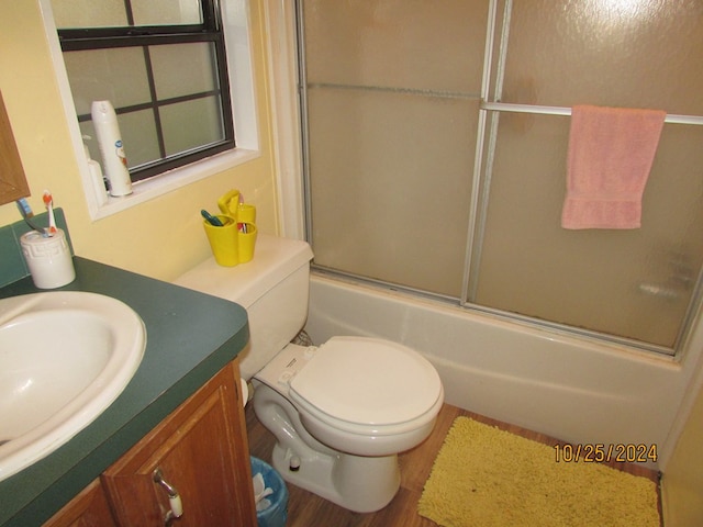 full bathroom featuring vanity, toilet, wood-type flooring, and bath / shower combo with glass door