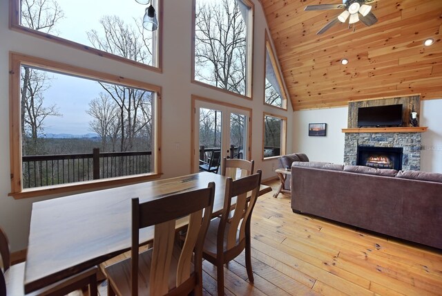 dining area featuring ceiling fan, high vaulted ceiling, a stone fireplace, french doors, and hardwood / wood-style floors