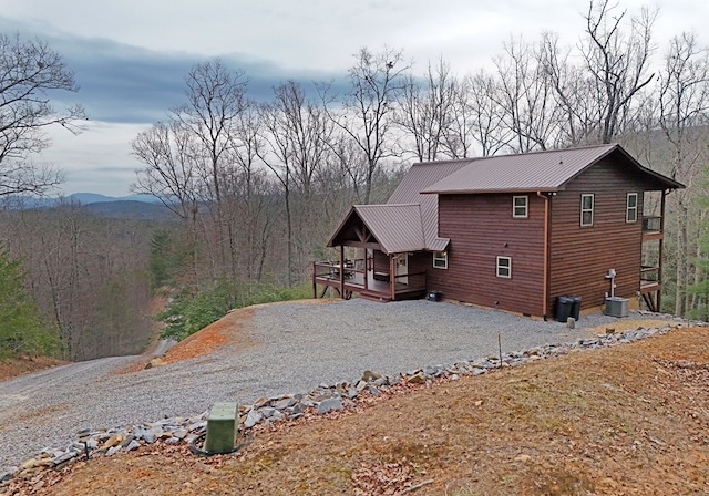 exterior space with metal roof, driveway, a view of trees, and a wooden deck