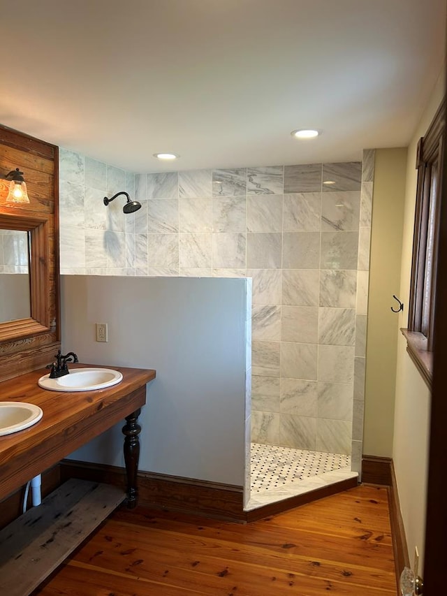 bathroom featuring double sink, wood-type flooring, and tiled shower