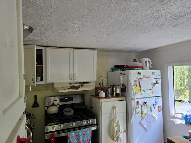 kitchen with stainless steel gas range, a textured ceiling, freestanding refrigerator, white cabinetry, and under cabinet range hood