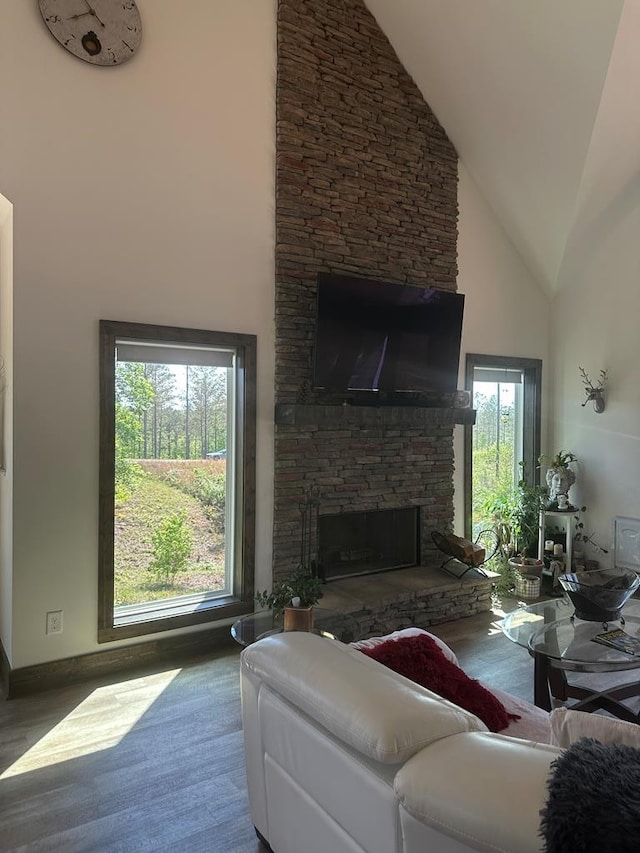 living room with high vaulted ceiling, a stone fireplace, and wood finished floors