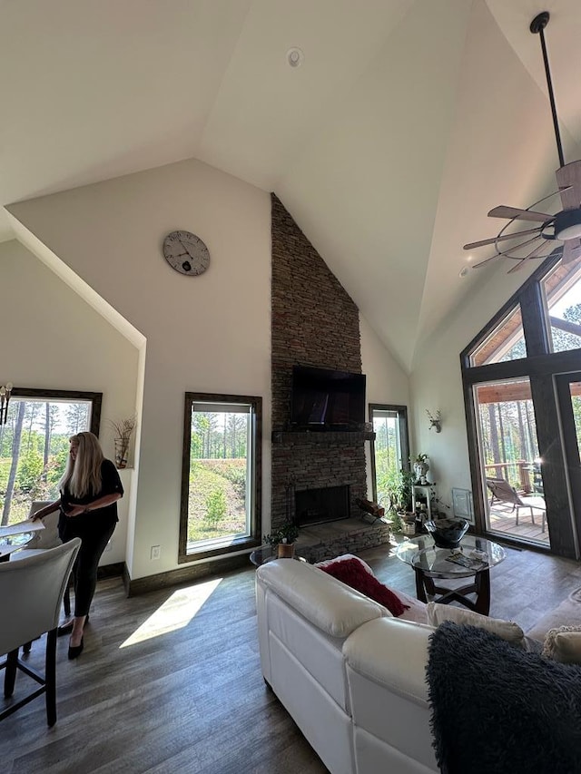 living area featuring a ceiling fan, a stone fireplace, wood finished floors, high vaulted ceiling, and baseboards