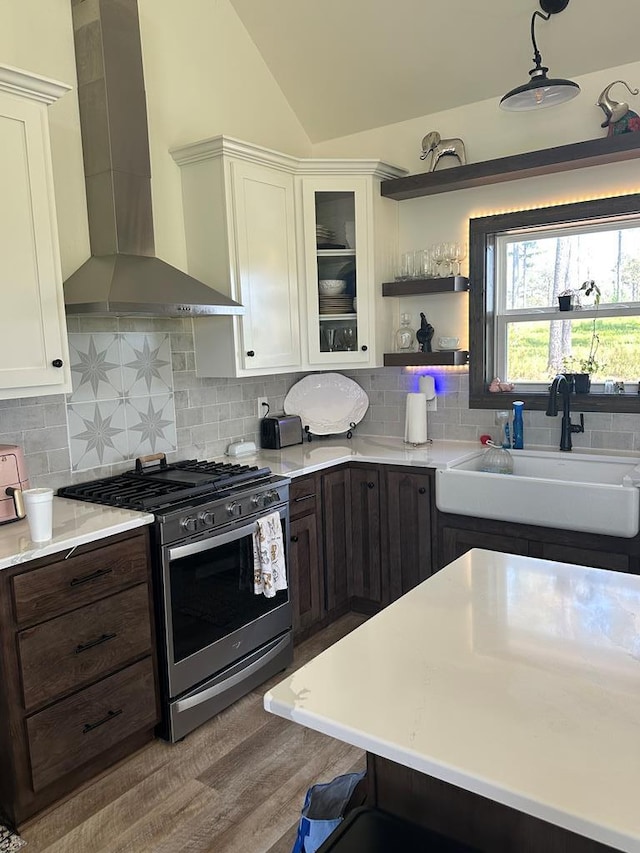 kitchen with light countertops, wall chimney exhaust hood, white cabinetry, a sink, and gas stove