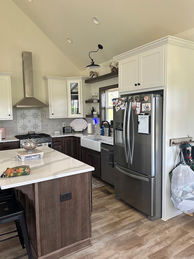 kitchen with lofted ceiling, wall chimney exhaust hood, white cabinetry, a sink, and stainless steel appliances