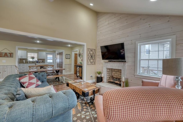 living room with high vaulted ceiling, recessed lighting, a fireplace, and wood walls