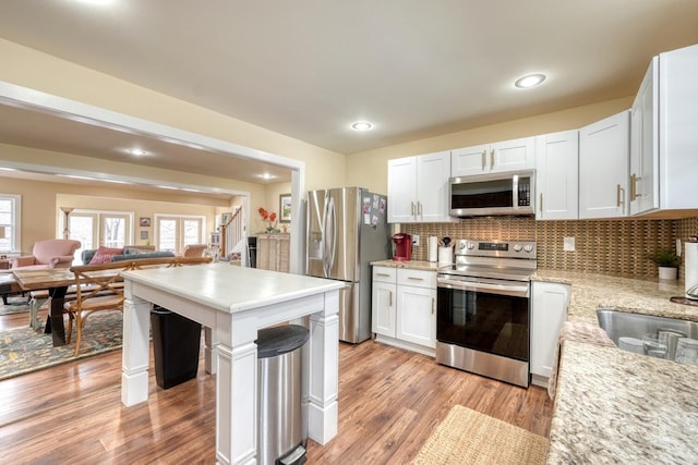 kitchen with light wood-style flooring, stainless steel appliances, white cabinets, open floor plan, and backsplash