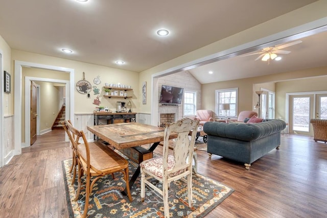 dining space featuring a fireplace, wainscoting, vaulted ceiling, wood finished floors, and stairs