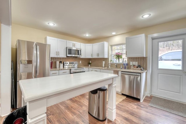 kitchen with appliances with stainless steel finishes, light countertops, light wood-style flooring, and tasteful backsplash