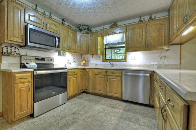 kitchen with appliances with stainless steel finishes, a sink, brown cabinets, light countertops, and a textured ceiling