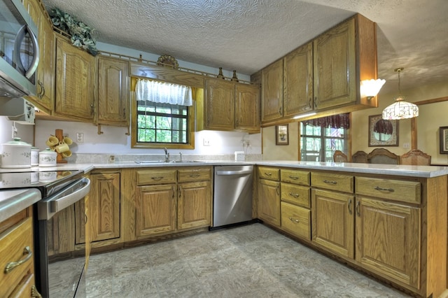 kitchen featuring appliances with stainless steel finishes, a sink, brown cabinets, a peninsula, and light countertops