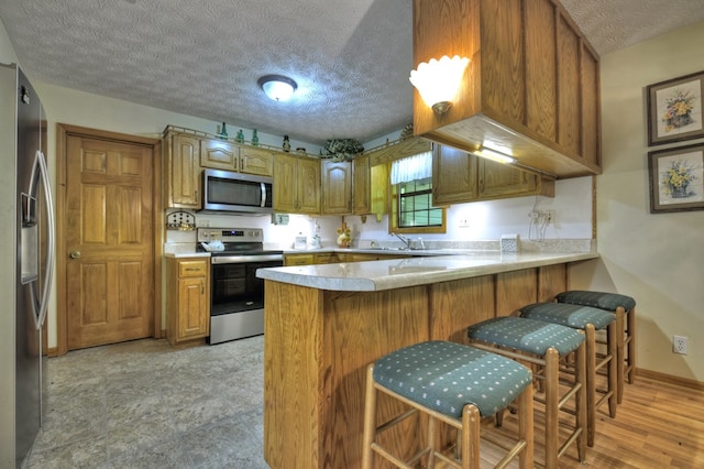kitchen featuring stainless steel appliances, a peninsula, a textured ceiling, light countertops, and brown cabinetry