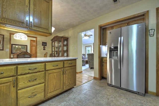 kitchen with stainless steel fridge with ice dispenser, brown cabinets, light countertops, a textured ceiling, and a ceiling fan