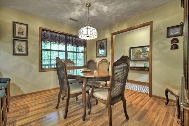 dining room featuring a chandelier, light wood-type flooring, baseboards, and a textured ceiling