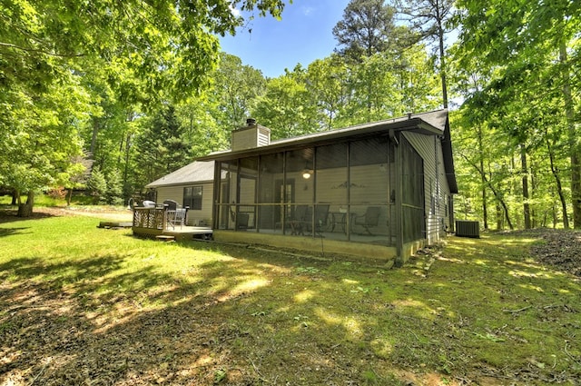 rear view of house featuring a sunroom, central AC, a chimney, a lawn, and a deck