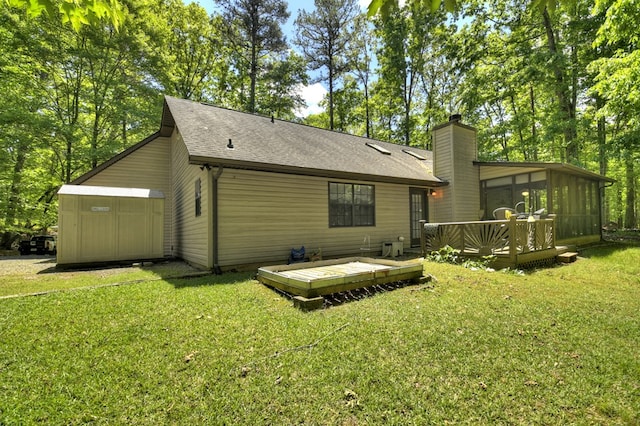 rear view of house featuring a sunroom, a wooden deck, a yard, a chimney, and a shingled roof