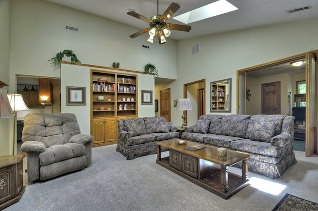 living room with carpet floors, high vaulted ceiling, ceiling fan, and a skylight