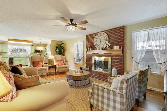 living room with sink, a textured ceiling, a brick fireplace, ceiling fan, and hardwood / wood-style flooring