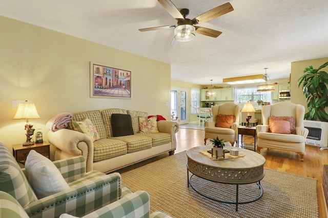 living room with a textured ceiling, light hardwood / wood-style flooring, heating unit, and ceiling fan with notable chandelier