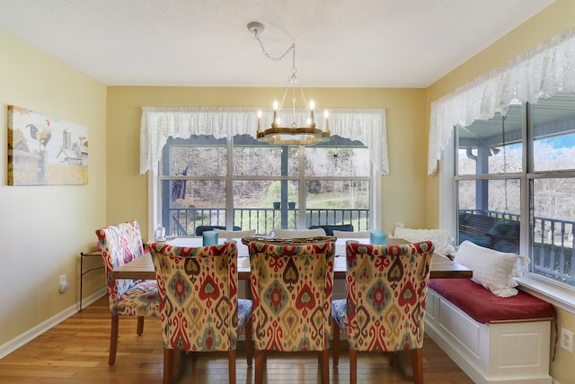 dining space with a textured ceiling, wood-type flooring, and an inviting chandelier