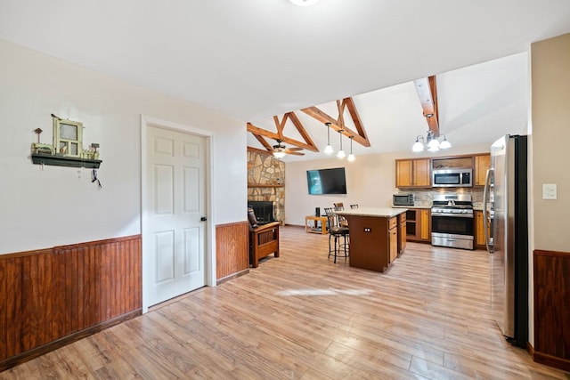 kitchen with vaulted ceiling with beams, hanging light fixtures, stainless steel appliances, a breakfast bar, and a center island