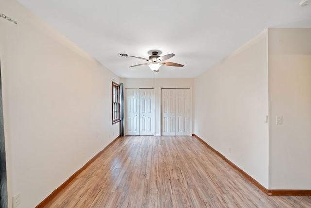 unfurnished bedroom featuring light wood-type flooring, ceiling fan, and two closets