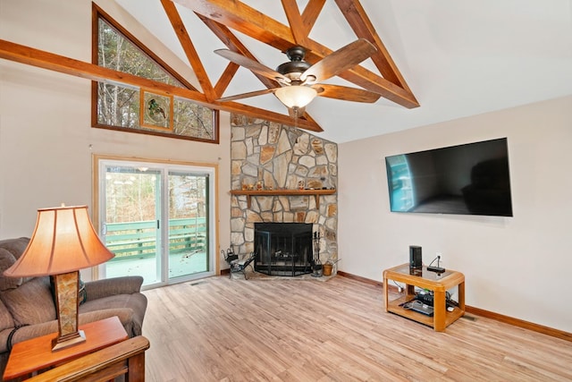 living room featuring ceiling fan, light hardwood / wood-style flooring, a stone fireplace, and beamed ceiling