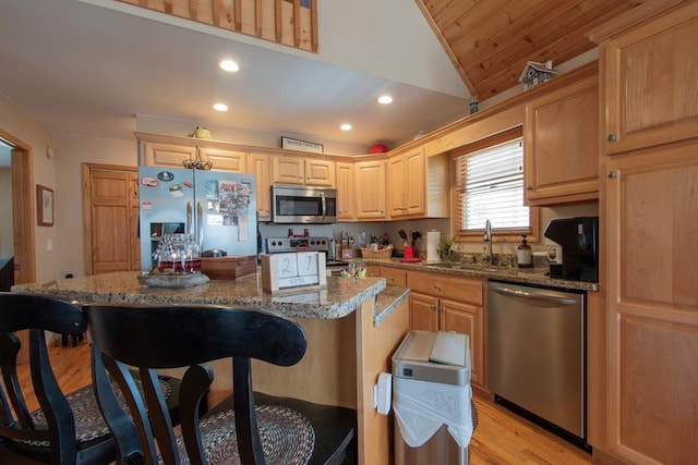 kitchen with lofted ceiling, sink, a kitchen island, light stone counters, and stainless steel appliances