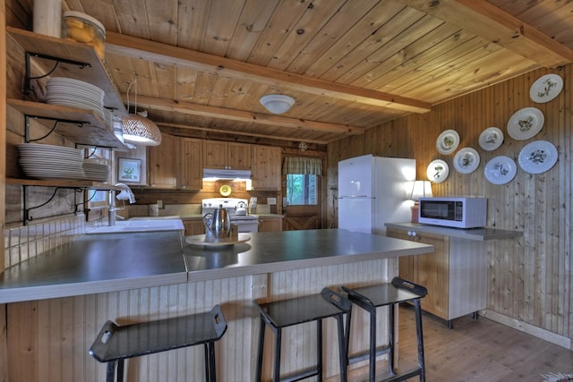 kitchen with sink, beam ceiling, white appliances, wooden walls, and light wood-type flooring