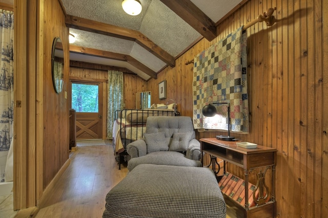 living area with a textured ceiling, vaulted ceiling with beams, wooden walls, and light hardwood / wood-style flooring