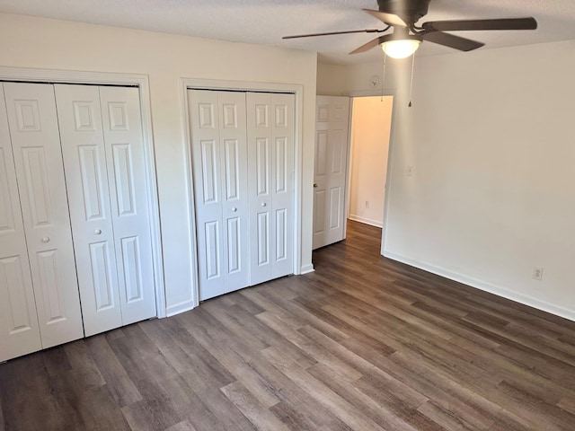 unfurnished bedroom with baseboards, two closets, wood finished floors, and a ceiling fan