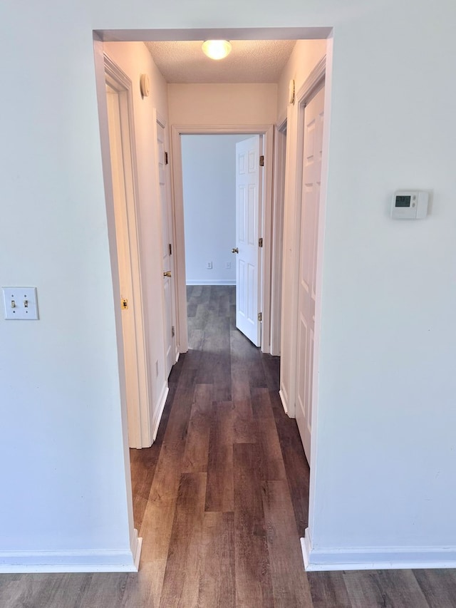 corridor featuring baseboards and dark wood-style floors